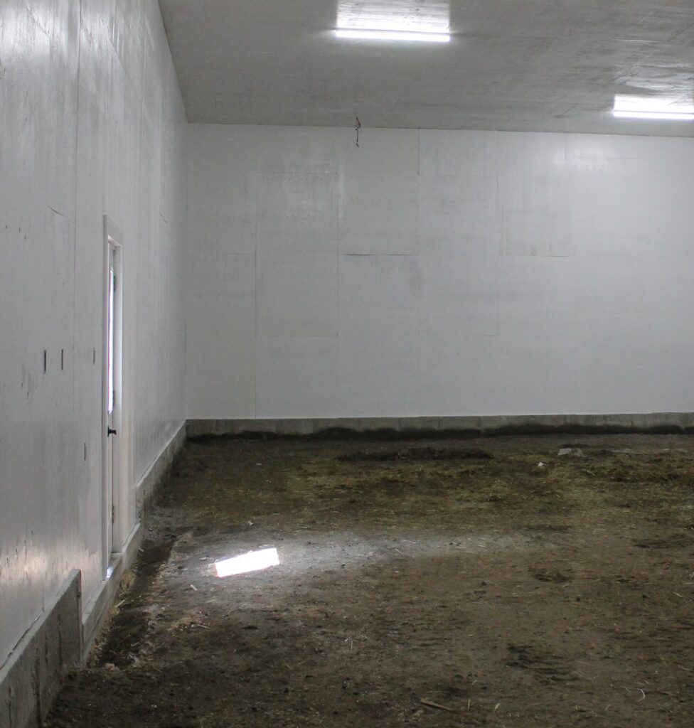 A freshly painted white room. Light is shining in onto the dirt ground.