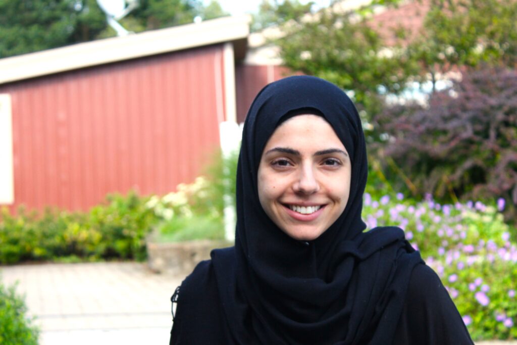 Fatima is wearing a black hijab and is smiling. The weather is mild and comfortable.